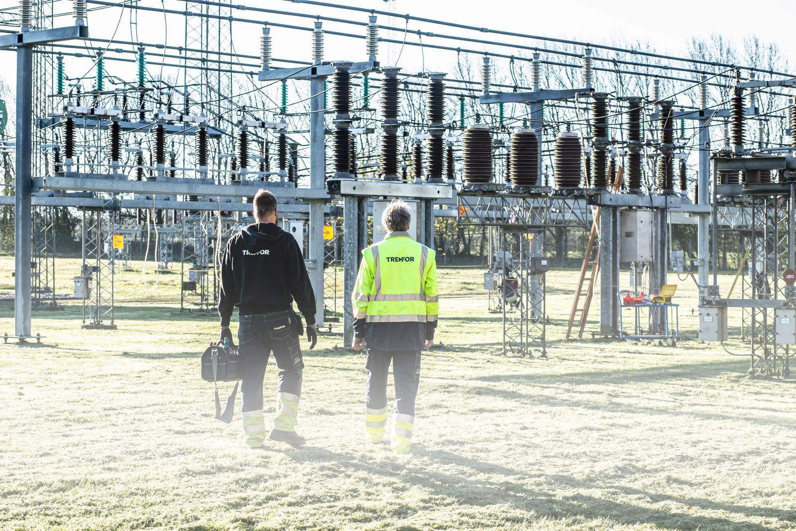 Deux travailleurs inspectent une sous-station électrique extérieure, mettant l'accent sur la sécurité et l'entretien.